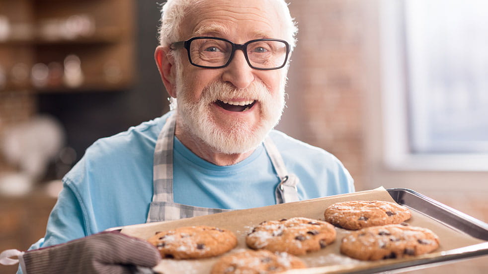 Loneliness at Christmas old man baking cookies smiling